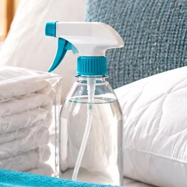 Atomizador transparente con tapa turquesa junto a almohadas